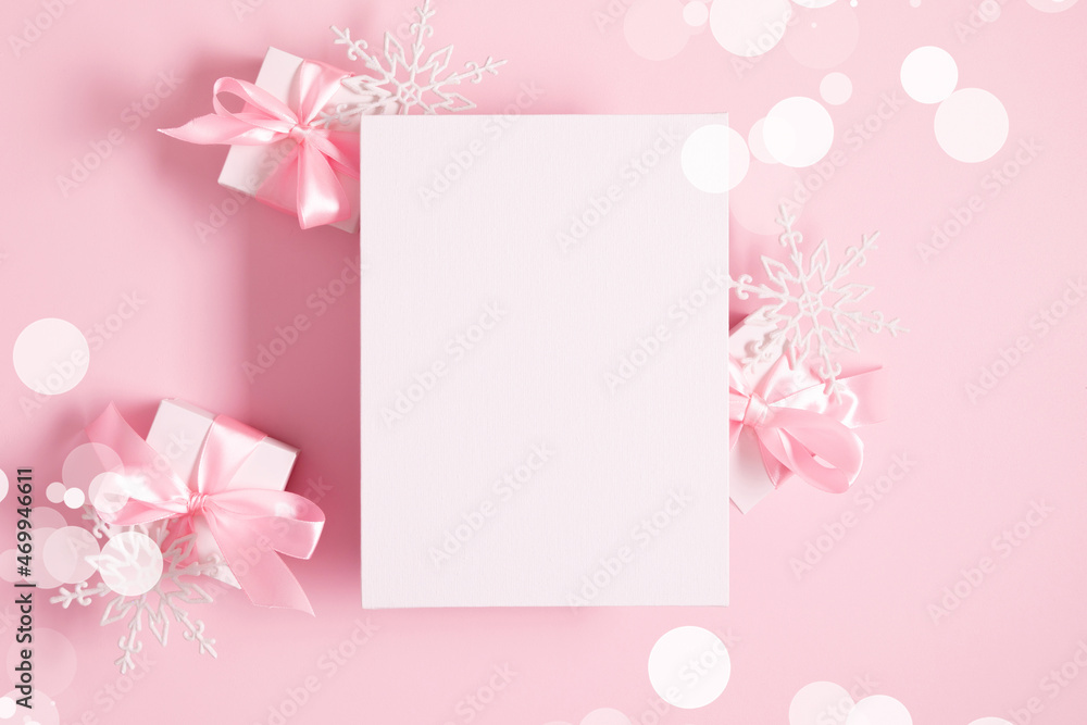 Christmas holiday composition. Blank white canvas mockup, gift, snowflake on pastel pink background. Xmas, winter, new year concept. Flat lay, top view, copy space