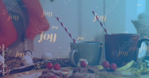 Image of joy text falling over christmas decorations and mugs of hot chocolate