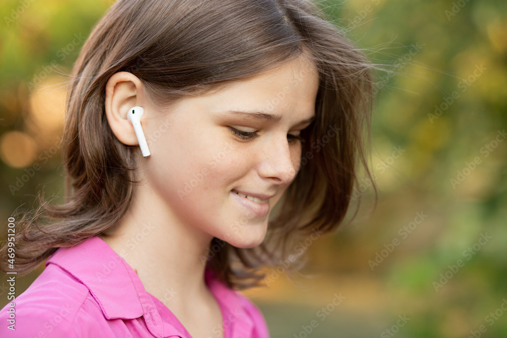 Close up portrait of lovely girl in pink listening to music through wireless earphones outdoors. Young girl smiling happy. Airpods. 