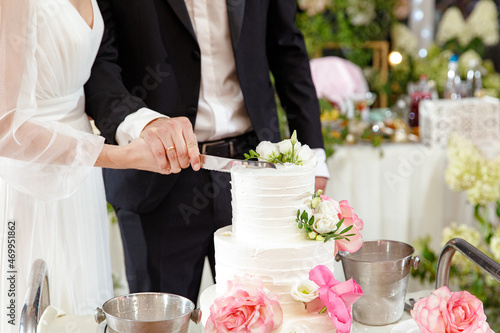 Bride and groom holding knife and cutting stylish white wedding cake with flowers. modern big wedding cake with pink and white roses