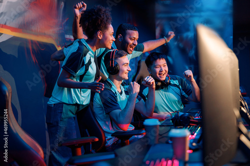 Multiracial cybersport gamers expressing success while raising hands up and smiling during participation in esports tournament in computer club photo
