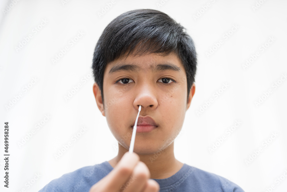 Asian boy self collecting nose swab for corona virus sample.Covid-19 laboratory test.Antigen test kit for rapid nose swab.Nasal swab is a test that takes a sample of cells from the nasopharynx. Asian boy self collecting nose swab for corona virus sample.Covid-19 laboratory test.Antigen test kit for rapid nose swab.Nasal swab is a test that takes a sample of cells from the nasopharynx.