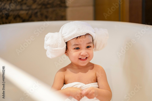 Asian cute baby girl in a bathrobe and hair wrapped in towel having fun in a bathtub