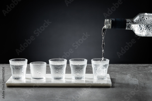 Pouring cold vodka into shot glass isolated on dark background. Selective focus. photo