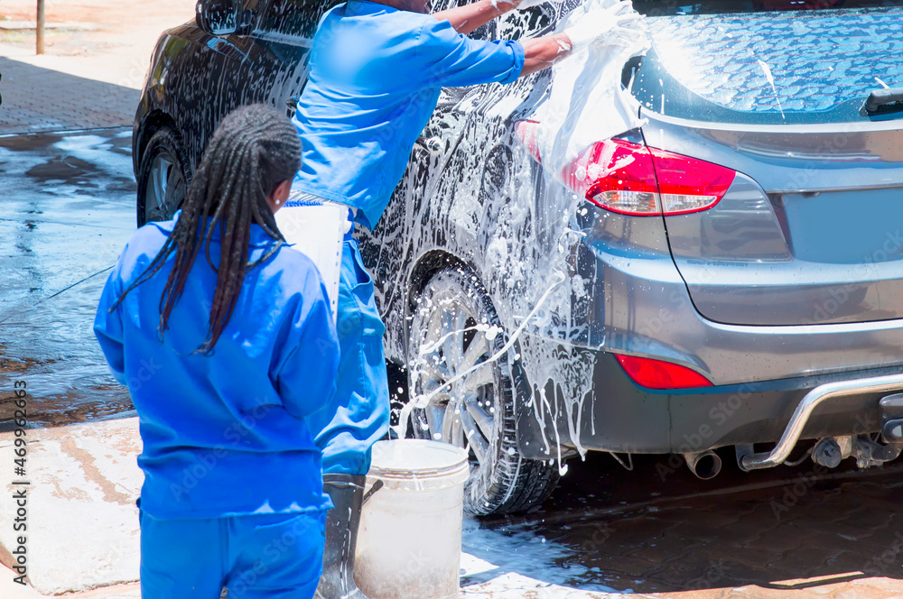 Obraz premium African man worker washing car's alloy wheels on a car wash