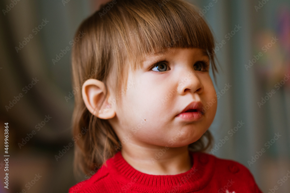 Child close-up portrait of little girl in red sweater. Waiting to receive presents for christmas and new year. Cute caucasian baby looking to the side