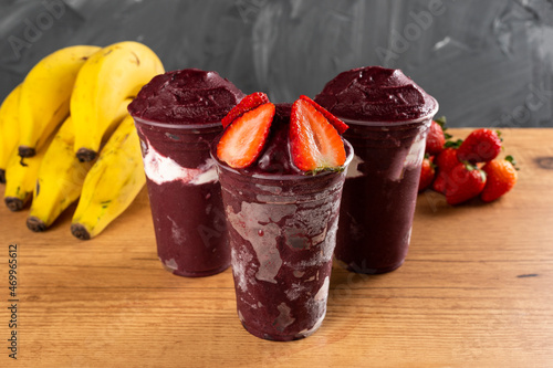 Fotografie Three Brazilian Frozen Açai Berry Ice Cream Smoothie in plastic cup with Strawberries and condensed milk