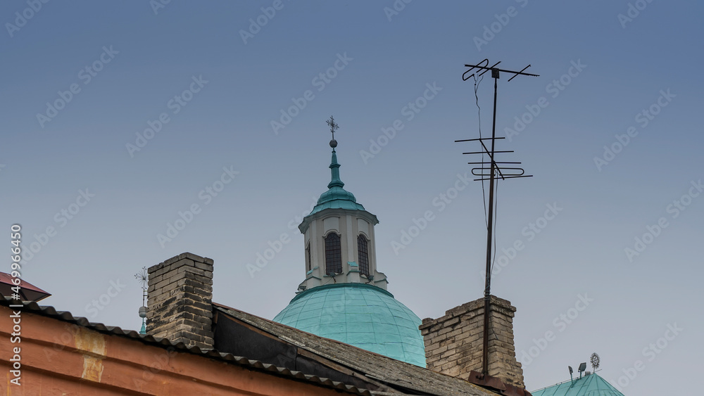 Catholic dom with cross viewed through television aerial antennae and apartment rooftops.