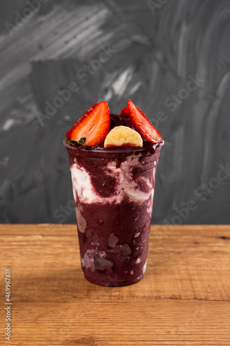Brazilian Frozen Açai Berry Ice Cream Smoothie in plastic cup with Strawberries, Bananas and Condensed Milk. On summer gray background. Front view for menu and social media