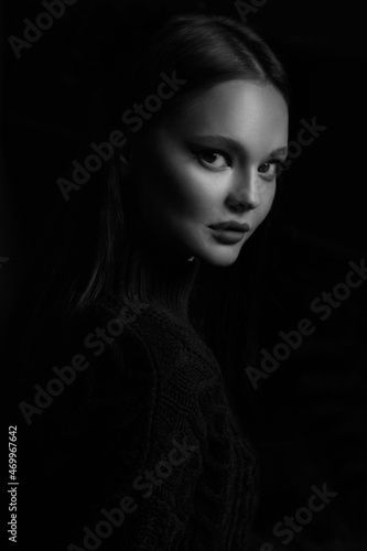 Black and white portrait of a beautiful brunette girl in a black sweater isolated on a black background.