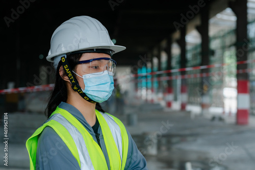 Portrait of an Asian female engineer Put on a brightly colored shirt. and wear a white safety cap standing with his arms crossed at the construction site