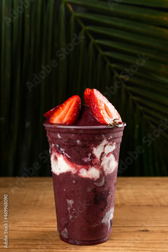 Brazilian Frozen Açai Berry Ice Cream Smoothie in plastic cup with Strawberries, Bananas and Condensed Milk. On summer leaves background. Front view for menu and social media