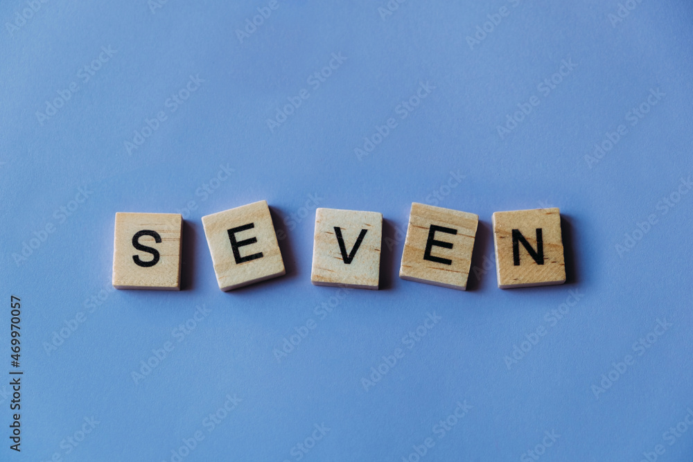 Number seven laid out from tiles in words. Wooden tiles on a blue background with letters. View from above. Copy space. Number seven laid out from tiles in words. Wooden tiles on a blue background with letters. View from above. Copy space.