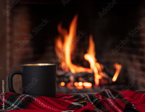 Christmas holiday cozy warm home. Cup of coffee on a sofa blanket, burning fireplace background.
