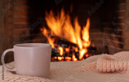 Cup of coffee on a sofa blanket, burning fireplace background. Christmas holiday cozy warm home