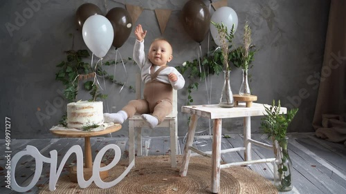 birthday one year old kid, toodler sitting on a chair near cake balloons, confetti pours on the boy child laughing, rustic style decor, happy birthday photo