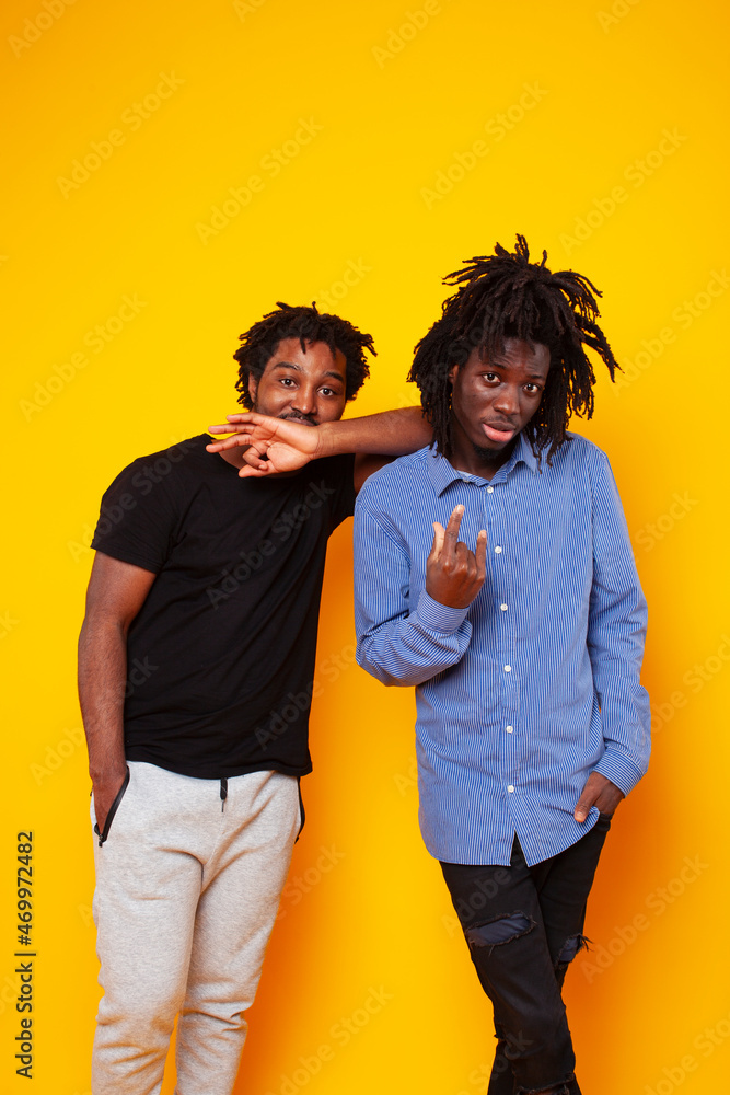 Obraz premium two african american guys posing cheerful together on yellow background, lifestyle people concept