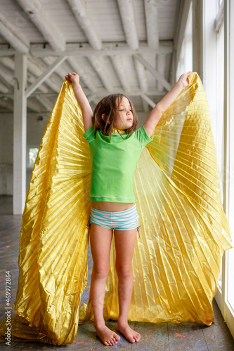 A small child stands by a window with golden wings and upraised arms photo