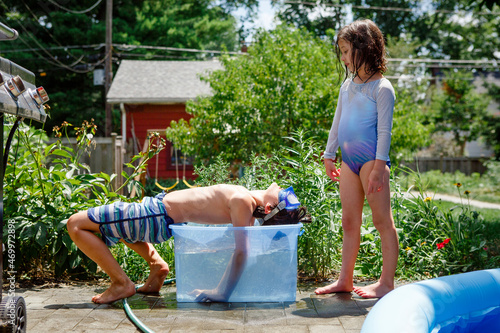 A boy and girl in bathing suits cool down in small tub of water