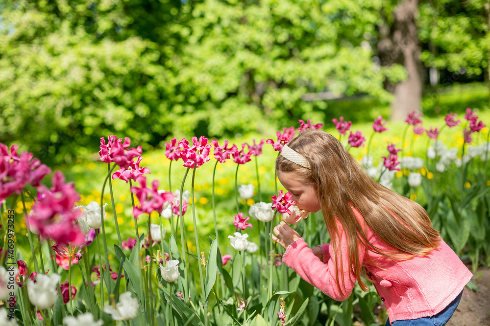 portrait of a very cute pretty girls blonde in a pink coat around the flower bed of tulips in the Park.Beautiful child smelling flowers on tulip fields. Child in tulip flower field portrait of a very cute pretty girls blonde in a pink coat around the flower bed of tulips in the Park.Beautiful child smelling flowers on tulip fields. Child in tulip flower field