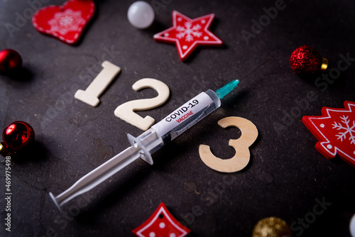Third covid vaccine dose and jab concept and numbers and Christmas decorations. Syringe is seen on table as a concept for the 3rd covid-19 vaccine dose, also called booster shot