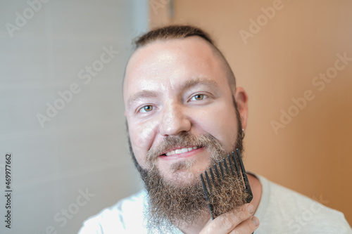 Caucasian man combing his beard while smiling. makeover concept