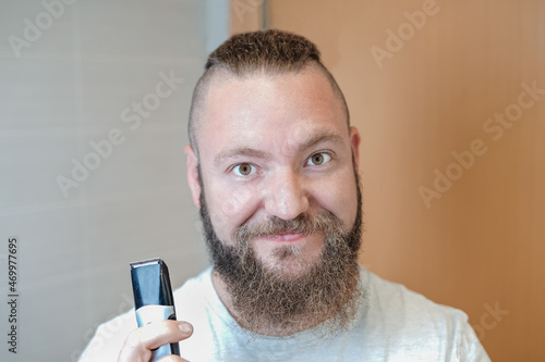 Caucasian man with long hair and beard before cutting his hair with an electric trimmer.
