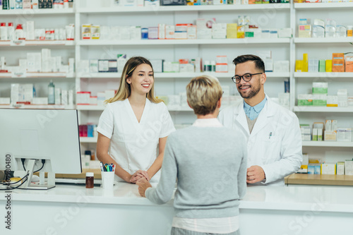 Two pharmacist giving prescription medications to senior female customer in a pharmacy photo