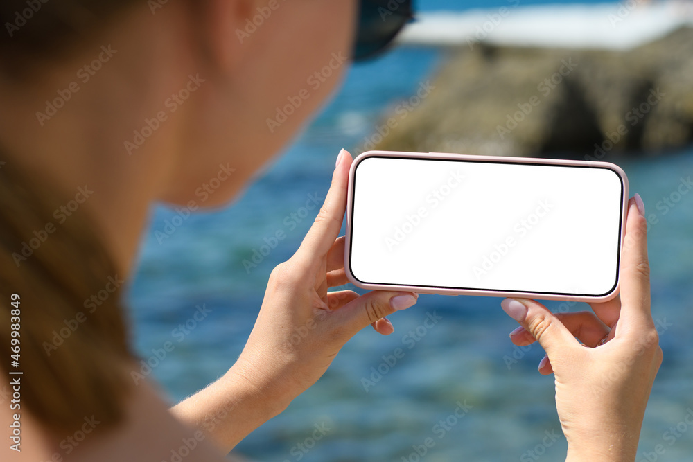 The girl holds horizontally a smartphone with a blank white display on the background of the sea.