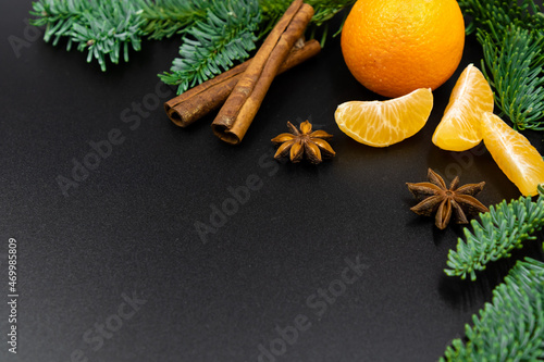 New Year's background. A branch of fir, tangerines and spices for mulled wine on a black background.