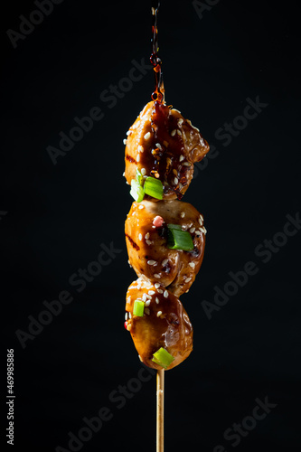 Skewer with chicken fillet drizzled with sauce on a black background.