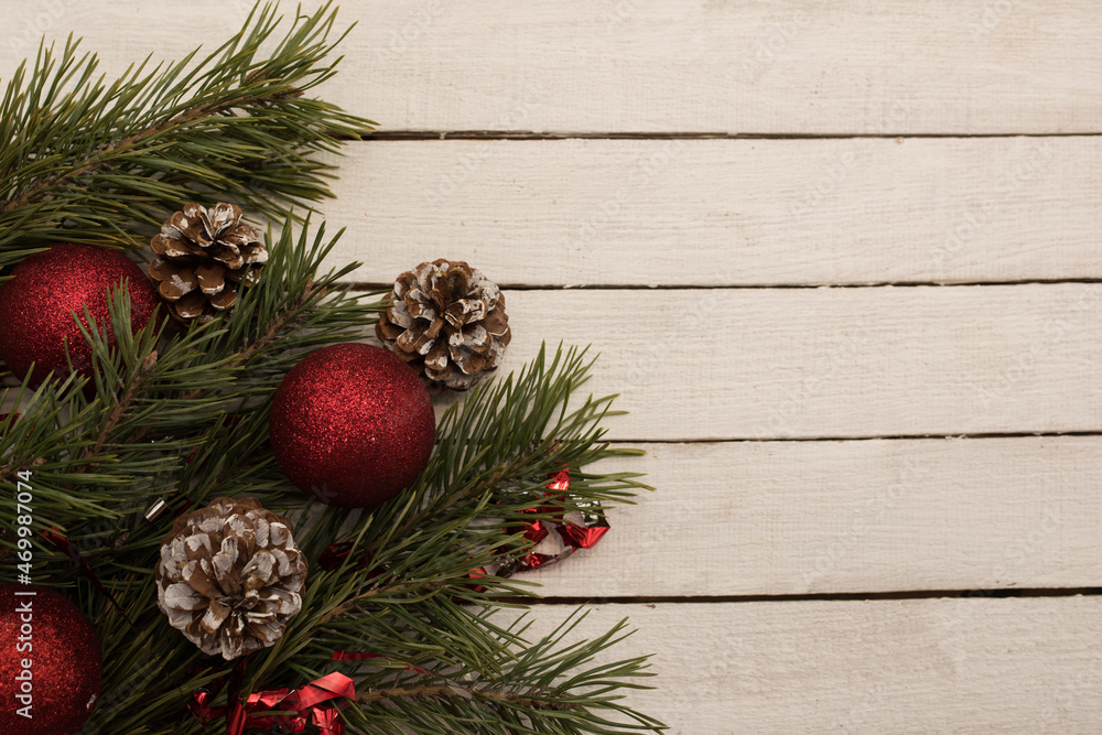 Red Christmas balls and cones on a green spruce branch on a white wooden background, top view, place for text.
