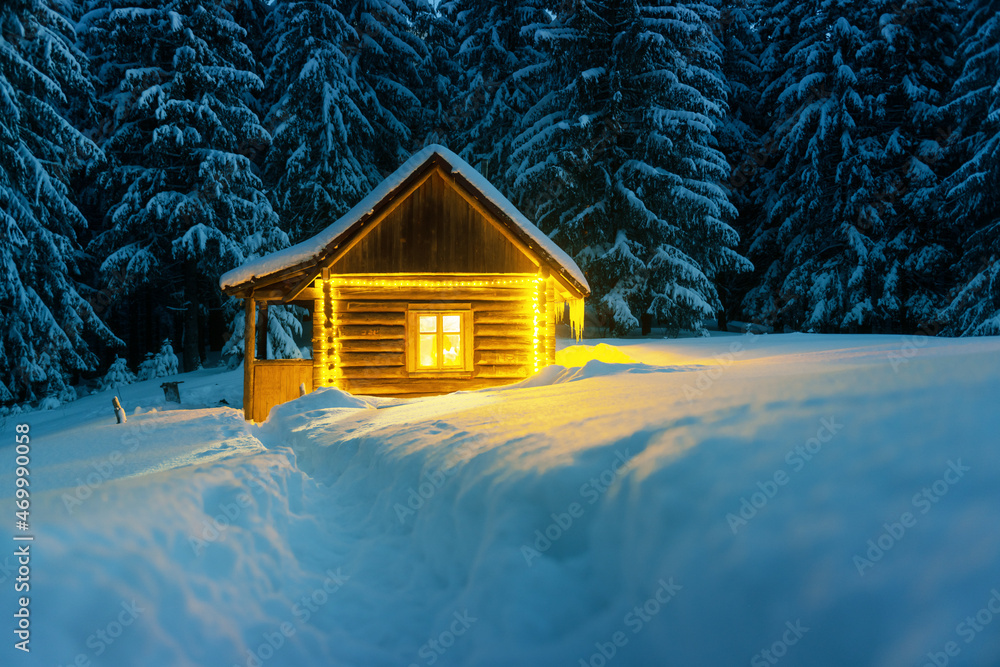 Fototapeta premium Fantastic winter landscape with glowing wooden cabin in snowy forest. Cozy house in Carpathian mountains. Christmas holiday concept