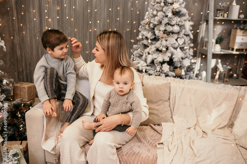 cute blonde mom with her sons is sitting on the couch in the room in a New Year's atmosphere