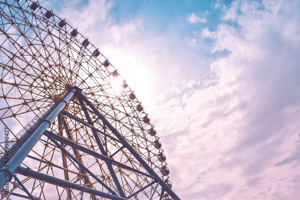 Ferris wheel in the amusement park photographed against the sun. Construction of the attraction with pink sky and clouds in the background. Adventure, holiday concept, conceptual