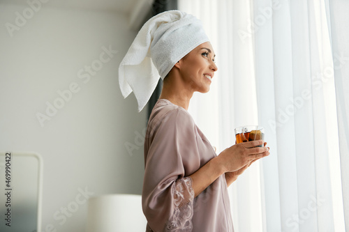 Tablou pe pânză Beautiful woman enjoys in cup of tea by the window at home.