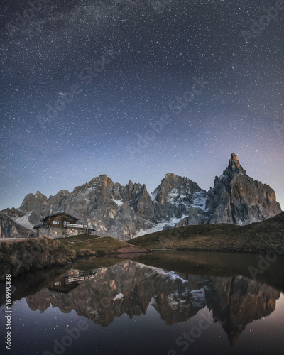 Incredible night landscape with a reflection of starry sky and mountains in a water of small lake in a popular tourist destination - Baita Segantini mountain refuge. Rolle Pass, Dolomites Alps, Italy photo