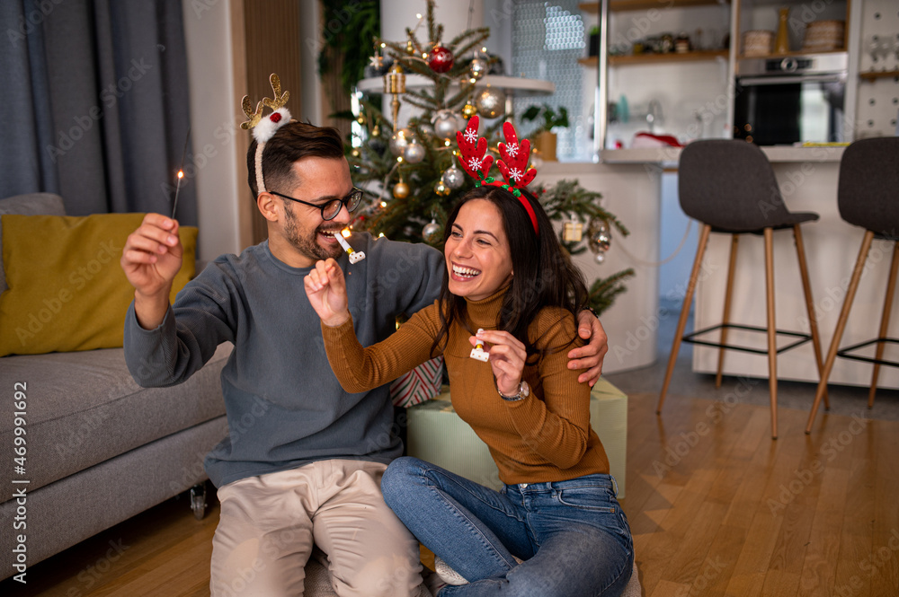 Portrait of a happy Caucasian young lovers having fun at home, celebrating winter holidays together, playing with Christmas sparkler ornaments and smiling Portrait of a happy Caucasian young lovers having fun at home, celebrating winter holidays together, playing with Christmas sparkler ornaments and smiling