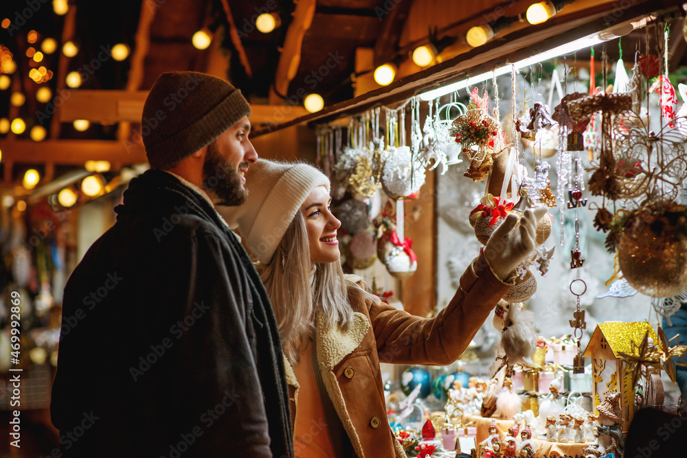 Christmas, winter holidays, vacation, travel, purchase conception: happy smiling couple shopping at festive street market, choosing gifts.  Outdoor night portrait. Copy, empty space for text
 - obrazy, fototapety, plakaty 