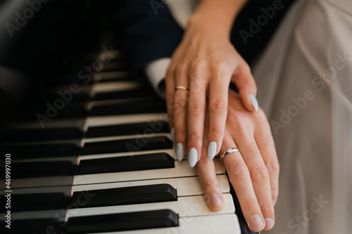 the hands of the newlyweds on the piano keys,
wedding engagement rings on fingers, close-up of couple's hands with rings