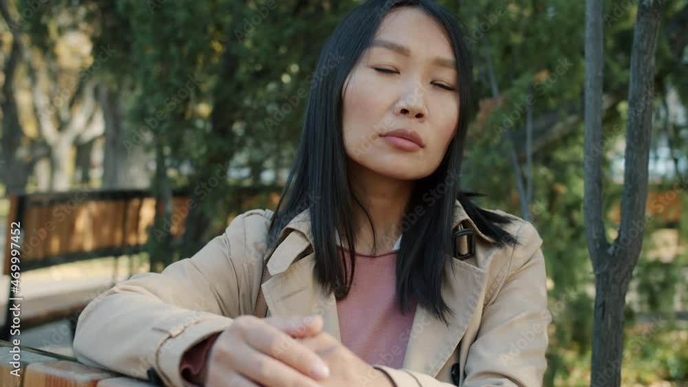 Portrait of serious young Asian business lady looking at camera sitting outside in city park wearing elegant clothing. People and urban background concept. Portrait of serious young Asian business lady looking at camera sitting outside in city park wearing elegant clothing. People and urban background concept.