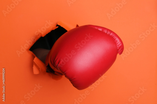 Man breaking through orange paper with boxing glove, closeup