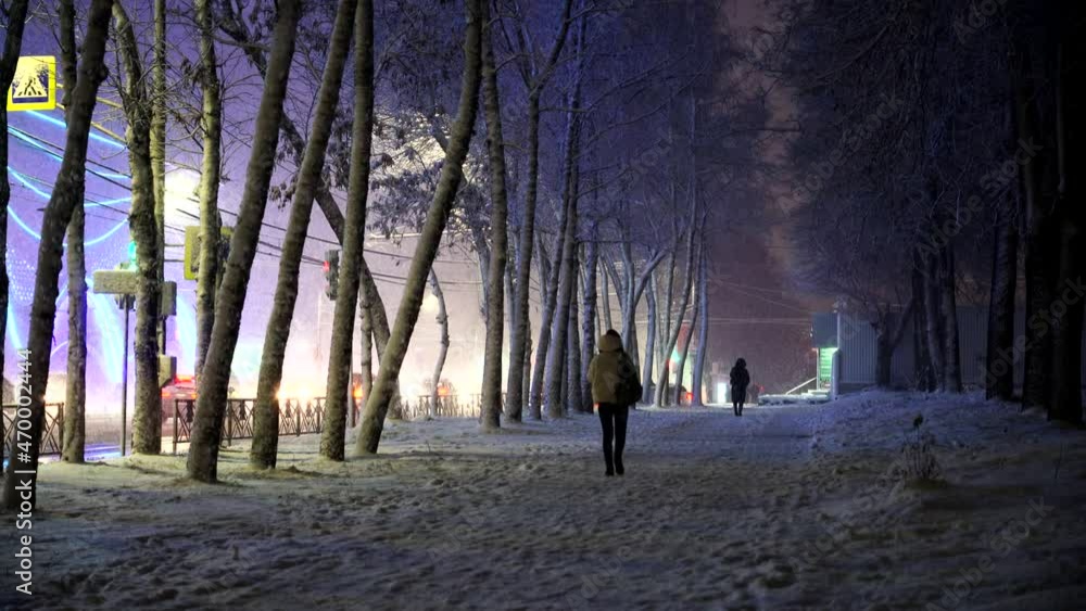 A girl walks along the sidewalk on a winter evening during a snowfall, a snow storm, cars drive along the road A girl walks along the sidewalk on a winter evening during a snowfall, a snow storm, cars drive along the road