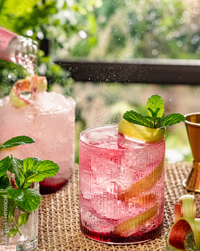rhubarb cocktail with tonic on rug backgroun styled in garten, action shot, sun light