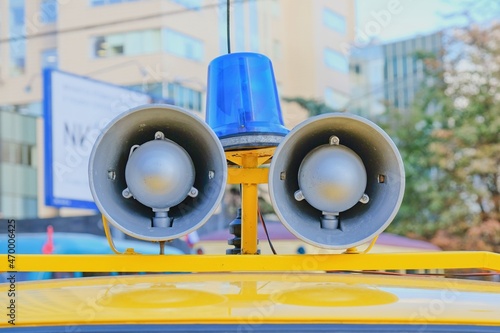Focus on details of retro police car with a megaphone and flashing blue siren light mounted on top. Loud-hailers on police car for message information at emergency. Vintage loudspeakers on car roof.