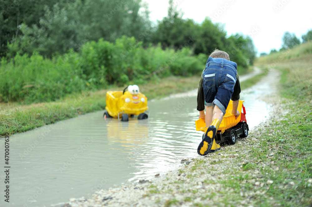 A little boy is playing with toy cars in a huge puddle.
A little boy is playing with toy cars in a huge puddle.