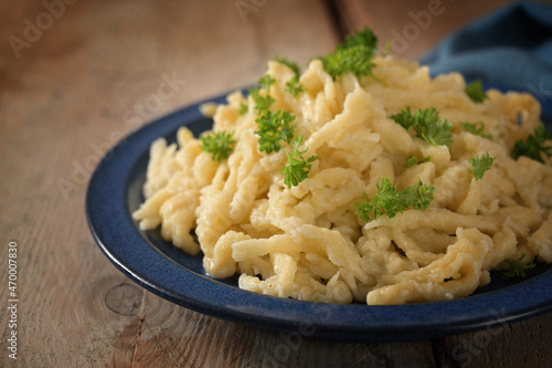 Homemade spaetzle, German egg noodles with cheese served with parsley garnish on a blue plate and a rustic wooden table, selected focus