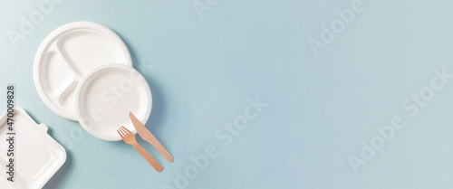Compostable or biodegradable dinnerware flat lay composition with copy space, horizontal banner format with copy space. Paper plate, food containers, wooden fork, knife on blue. Eco-friendly concept