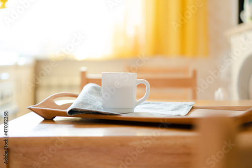 White coffee mug with napkin on table in real kitchen interior with bright natural sunlight