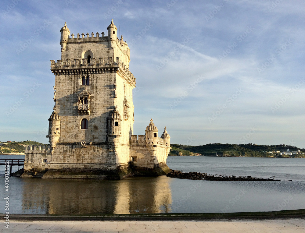 Belém Tower in Lisbon, Portugal, reflecting on Tagus river's waters, blue sky, sunny day, horizontal image